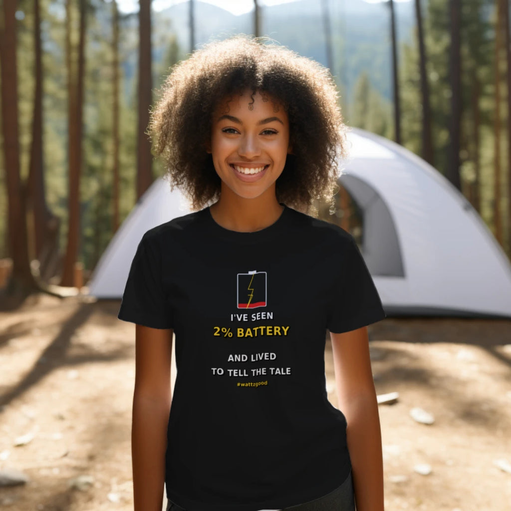 Woman at a campsite wearing the black Wattz Good "I've Seen 2% Battery and Lived to Tell the Tale" EV graphic tee
